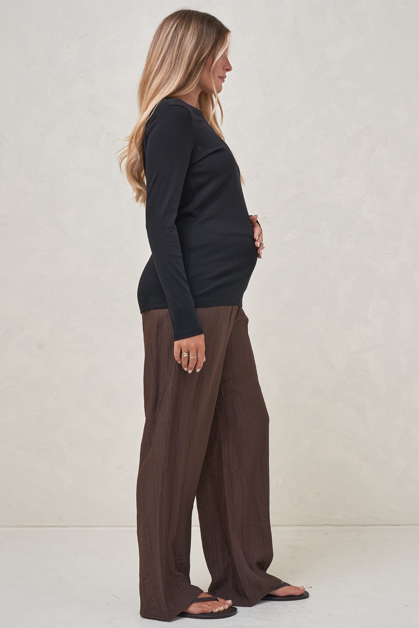 Black long sleeve maternity top side view showing the bump worn out over brown maternity pants